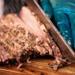 Barbecue brisket being expertly sliced by a gloved hand on a wooden cutting board.
