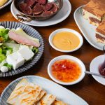 Close-up of an assorted Turkish meal spread with salad, cake, sauces, and tea on a wooden table.