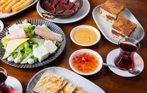 Close-up of an assorted Turkish meal spread with salad, cake, sauces, and tea on a wooden table.