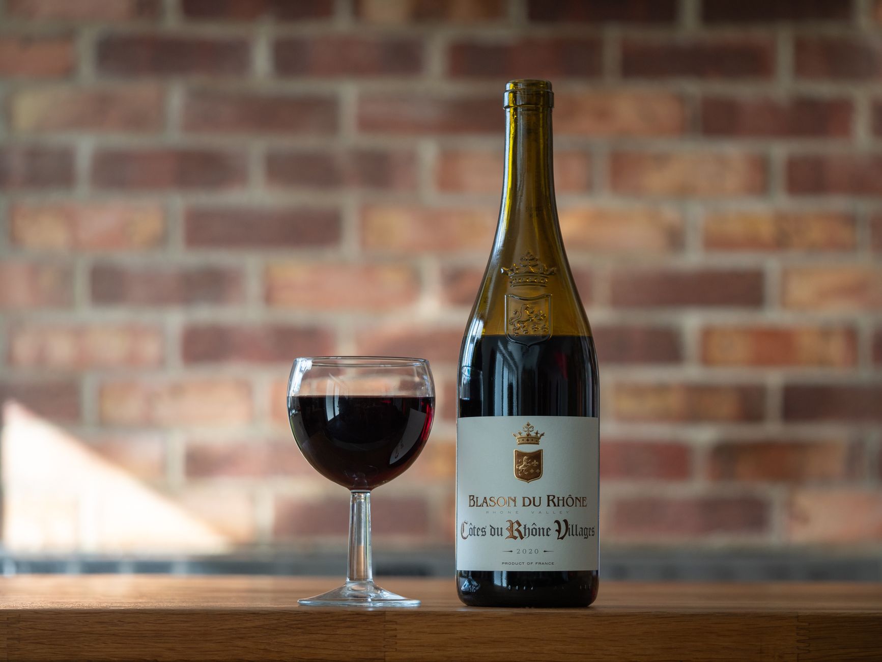 A sophisticated still life showcasing a bottle and glass of red wine against a brick background.
