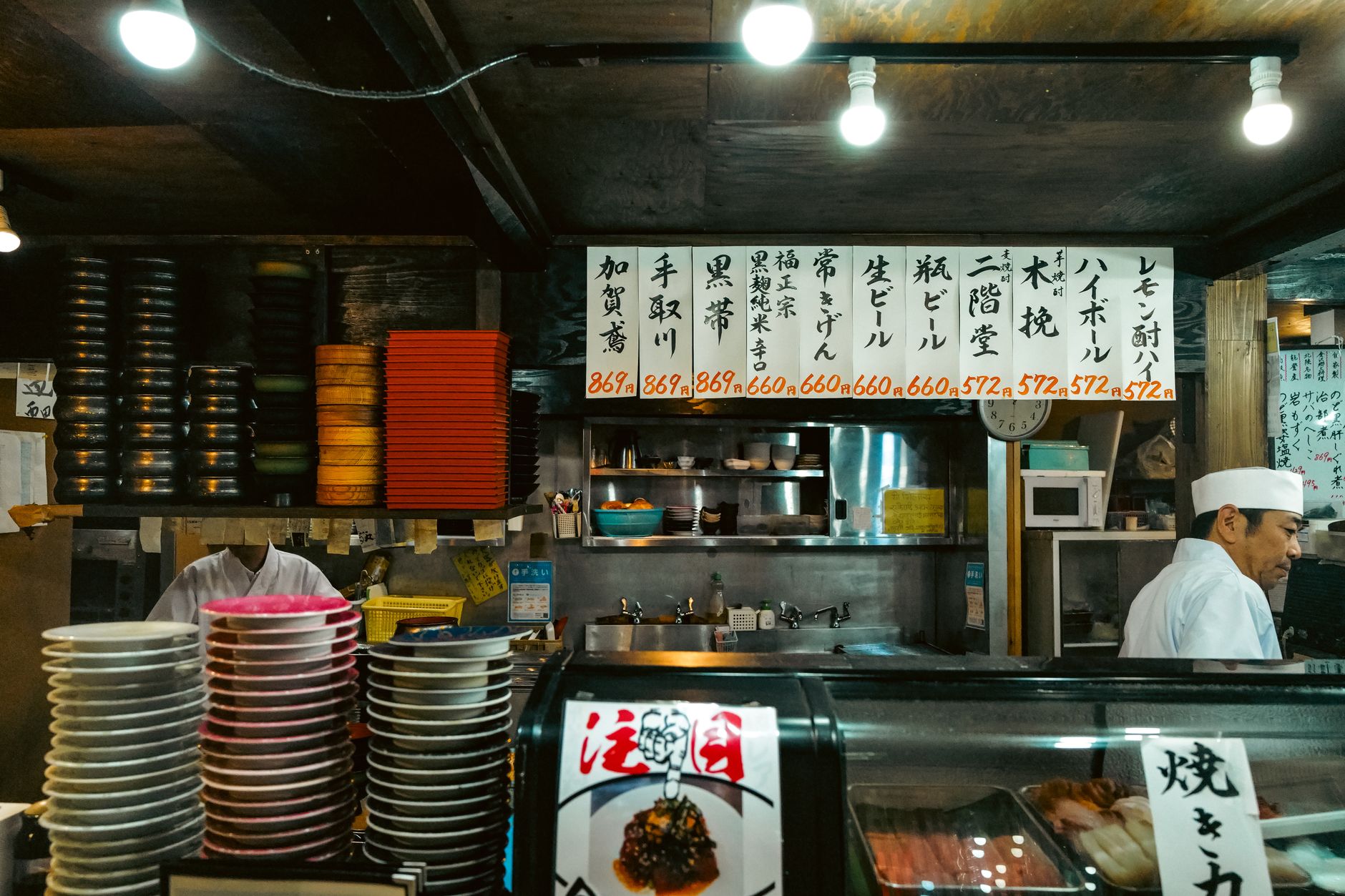 Colorful interior of a traditional Japanese sushi bar with chef and stacked plates.