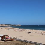 A stunning beach view of Portimão, Portugal, featuring golden sand and the blue ocean under a clear sky.