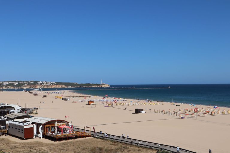 A stunning beach view of Portimão, Portugal, featuring golden sand and the blue ocean under a clear sky.