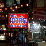 A bustling urban street at night with illuminated signs and vibrant market life.