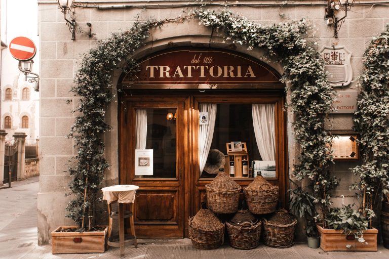 Exterior of cozy Italian restaurant with wooden door and entrance decorated with plants
