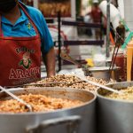 A street vendor in Guanajuato, Mexico serving various Mexican corn dishes from large pots outdoors.