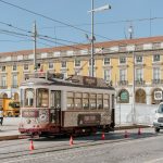 A classic tram on Lisbon's city street beside historic yellow architecture.