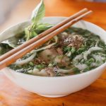 Delicious Vietnamese pho with fresh herbs and beef in a ceramic bowl, served with chopsticks.